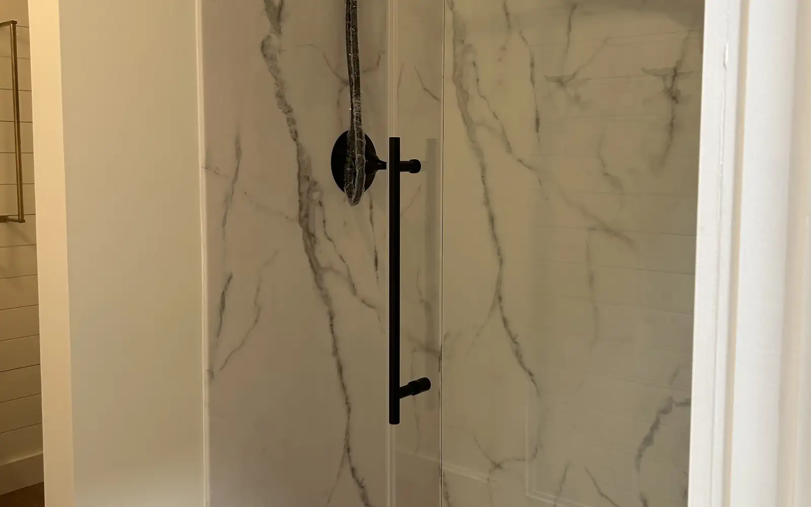Marble-look walk-in shower behind a streak-free sliding glass door with a black handle